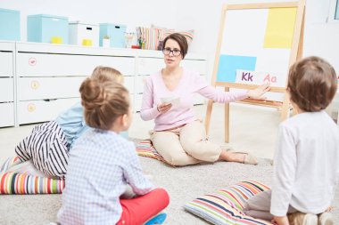 Beyaz tahta tarafından katta oturan ve küçük gösterilen ciddi orta yaşlı öğretmen İngilizce alfabenin harfleri çocuklar