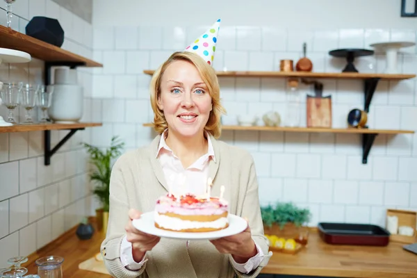 彼女のゲストのため自分で作ったケーキを持って誕生日キャップで笑顔の女性 — ストック写真