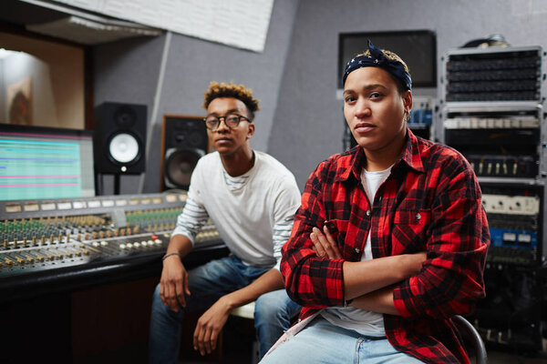 Two young colleagues sitting in studio of audio recording by soundboard