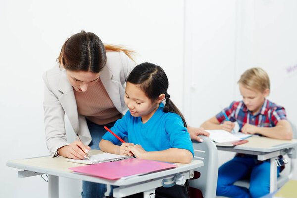 Молодой учитель проверяет заметки умной школьницы во время индивидуальной работы на уроке
