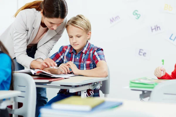 Teacher pointing at notes in pupil copybook while explaining him some mistakes