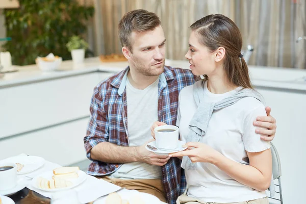 年轻人拥抱他的妻子与杯茶在早餐和她说话 — 图库照片