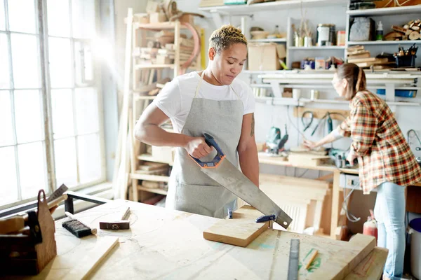 Mujer Joven Delantal Aserrando Madera Con Colega Trabajando Segundo Plano — Foto de Stock