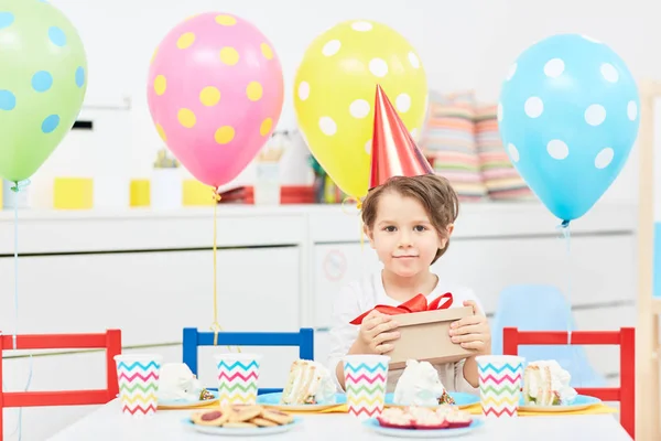 Menino Pacote Tampão Aniversário Segurando Com Presente Enquanto Sentado Mesa — Fotografia de Stock