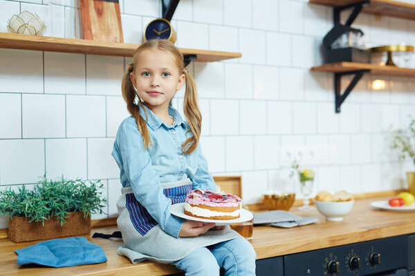 Pretty little girl sitting in the kitchen with tasty homemade cake for guests