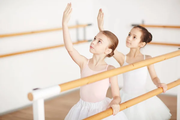 小群小女孩在芭蕾礼服看他们举起的手 当训练在教室时 — 图库照片