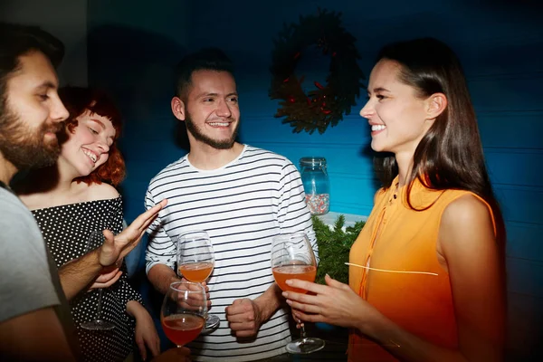 Happy young friends with refreshing drinks enjoying talk at party in club or restaurant