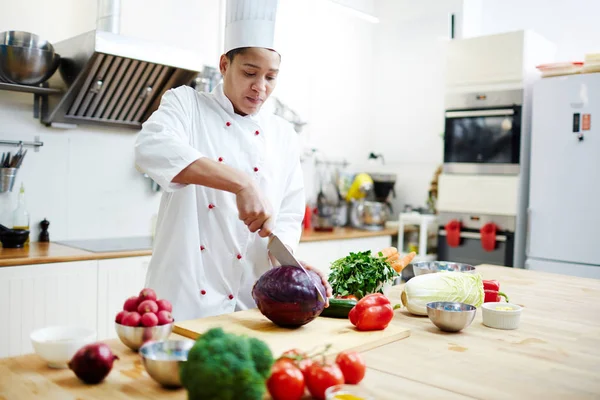 Joven Chef Uniforme Cortando Repollo Fresco Dos Mitades Mientras Prepara — Foto de Stock