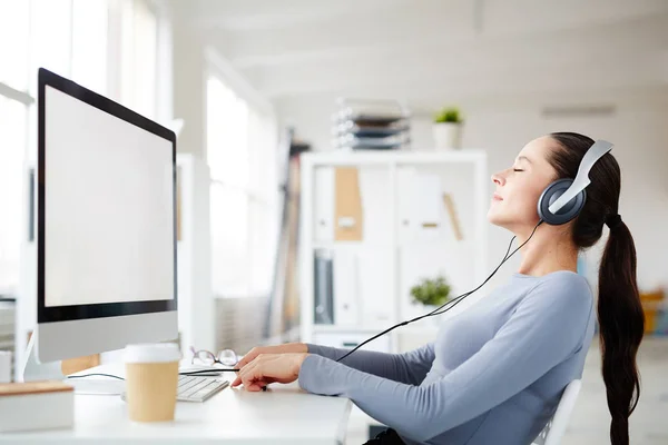 Happy young office worker taking pleasure in listening her favorite relaxing music in headphones at break