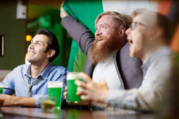 爱尔兰足球迷与国旗看电视在酒吧通过啤酒玻璃广播 — 图库照片