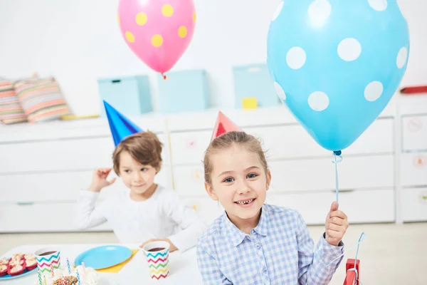 微笑的孩子与蓝色气球看照相机在生日聚会 而坐由节日桌 — 图库照片