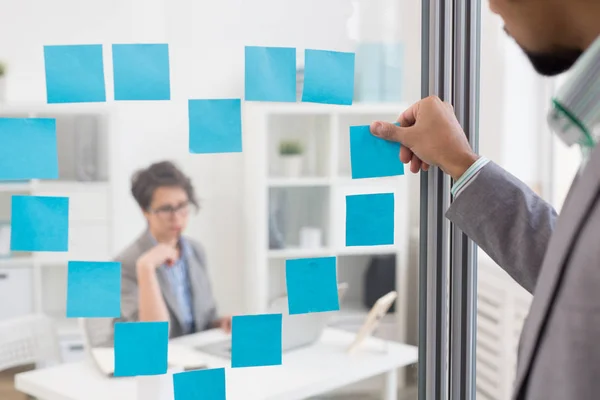 办公室工作者黏附 Notepapers 以心脏的形式在透明板与他的女性同事里面 — 图库照片