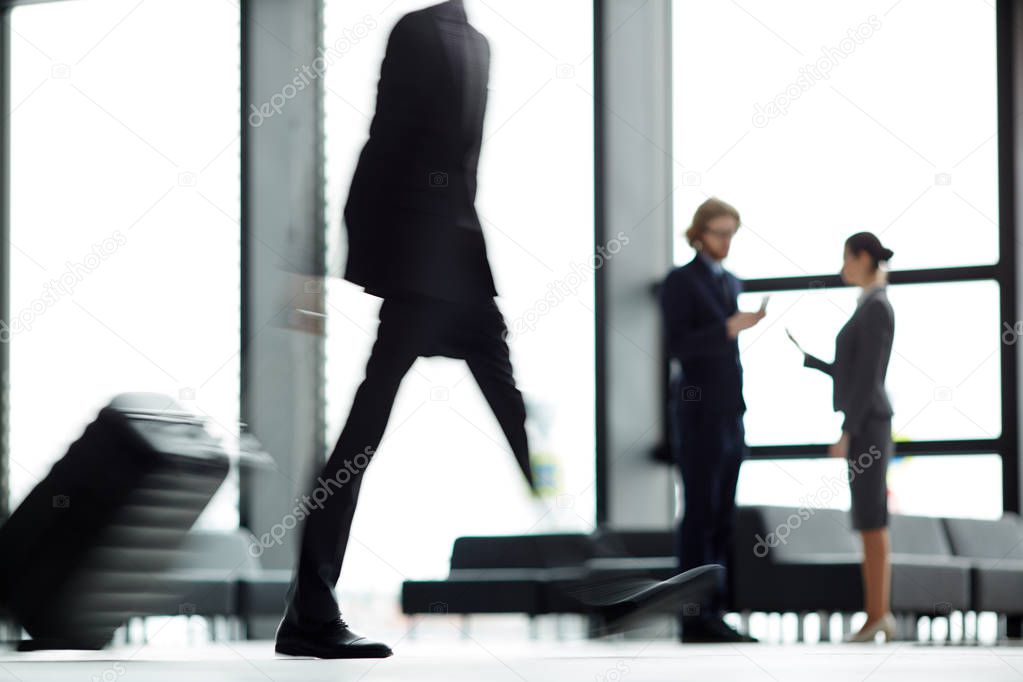 Blurry motion of contemporary business traveler with baggage walking down airport lounge