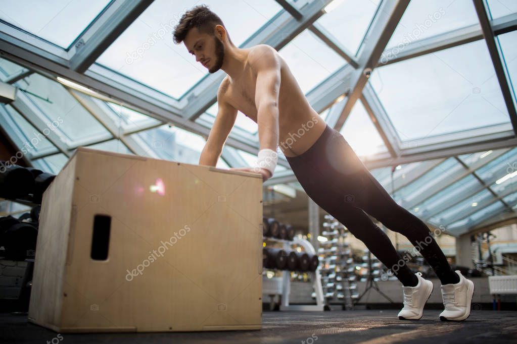 Sporty guy pushing up with his hands on jumpbox while training in crossfit club