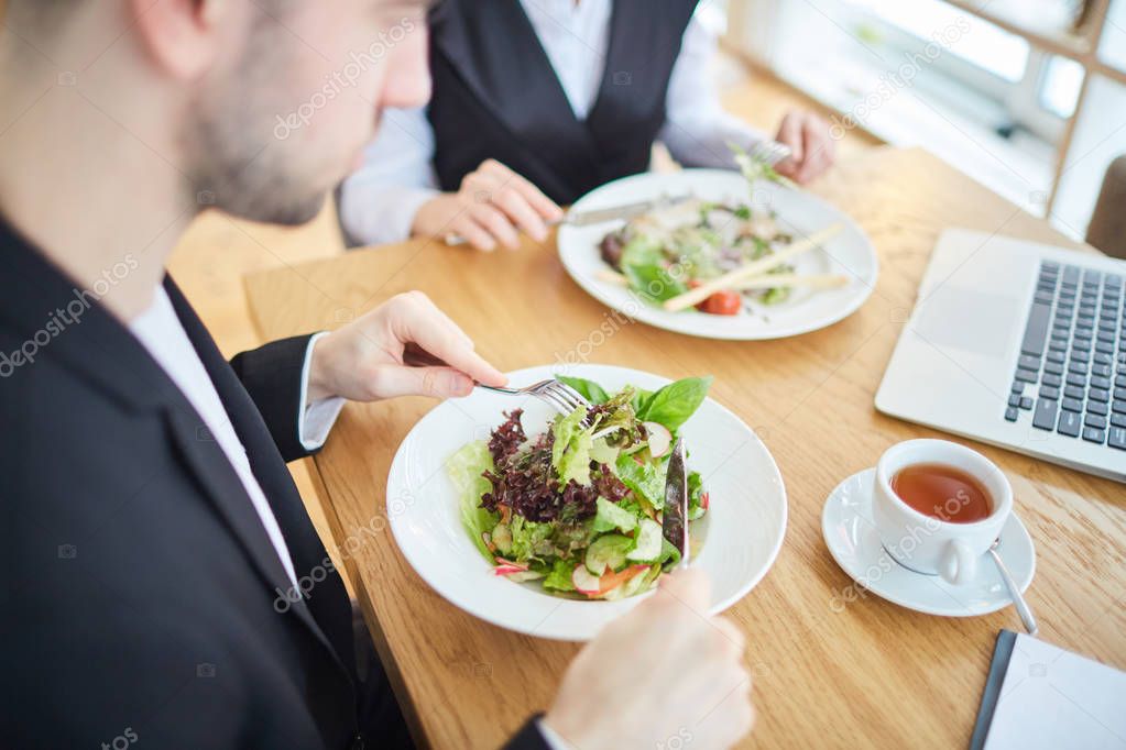 Fresh vegetable salad on plates of two employees networking during lunch in cafe