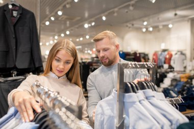 Gençler boş zamanlarında büyük ticaret merkezlerini ziyaret ederken askılarda asılı tişört koleksiyonuna bakarlar.