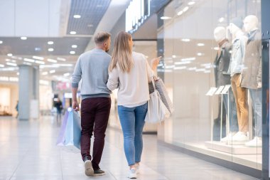 Alışveriş merkezinde vakit geçirirken mağazanın vitrinindeki yeni erkek günlük kıyafet koleksiyonuna dikkat eden genç müşteriler.