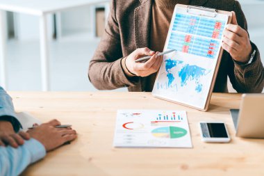 İki genç ekonomistten biri mali belgeye işaret ederken, meslektaşının şemasını veya masasını anlatıyor.