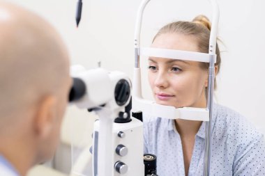 Klinikte ya da hastanede görme yeteneğini özel optometrik cihazlarla kontrol ettiren genç bir kadın.