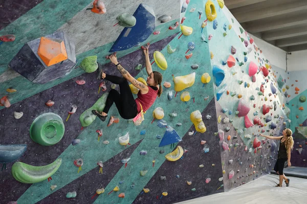 スポーツ用具の前でマットの上に立つ他の女性の背景に登る練習をしている若いアクティブな女性の一人 — ストック写真