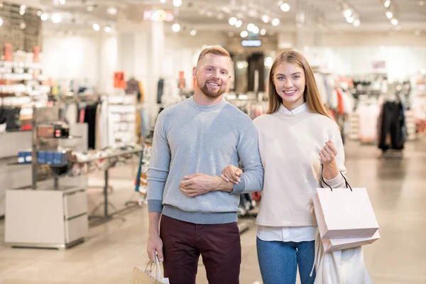 陽気若いショッピングカップルでジーンズとプルオーバーの中に立ってカメラの前に部門 — ストック写真