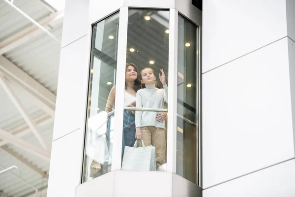 若い母親と娘は何かを話し合いながらエレベーターで上に移動しながらブラックフライデーショッピングモールで — ストック写真