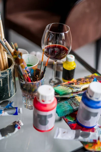 画家の職場で絵筆や様々な絵具やガッシュの間の赤ワインのガラス — ストック写真