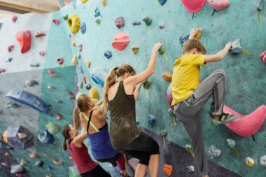 Genç sporcu kadınlar ve okul çocukları duvarlara tırmanırken küçük kayaları tutuyorlar.