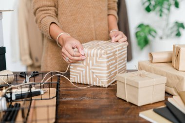 Genç bir kadın, Noel hediyelerini ahşap masadan hazırlarken ipliklerle sarmalanmış hediye kutusunu hazırlıyor.