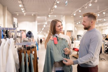 Alışveriş merkezinde alışveriş yaparken gri örgü kazağı göğüs göğüse gezdirip erkek arkadaşına bakan mutlu kız.