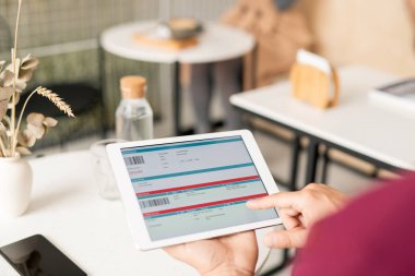 Genç adam, masadaki elektronik doküman üzerinde kaydırma yaparken dijital tablet görüntüsünü işaret ediyor
