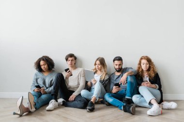 Akıllı telefonları ve dokunmatik ekranları olan bir grup ciddi milenyum kuşağı duvarın yanında otururken aletlerin içinde kayıyor.