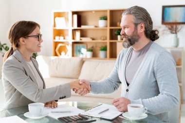 Olgun sakallı adam ve genç ve güzel meslektaşı anlaşmaya vardıktan sonra el sıkışıyorlar.