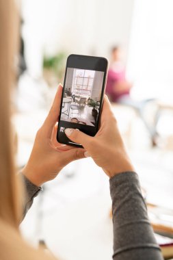 Akıllı telefonlu genç bir kadın modern kafenin içini çekerken boş vakitlerinde dinleniyor.
