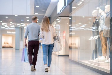 İstediklerini aldıktan sonra alışveriş merkezinin vitrininde hareket eden genç çiftlerin arka görüntüsü.