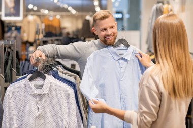 Genç çift erkek için yeni gömlek seçerken alışveriş merkezindeki giyim bölümünde yeni koleksiyon ile askıda duruyor.