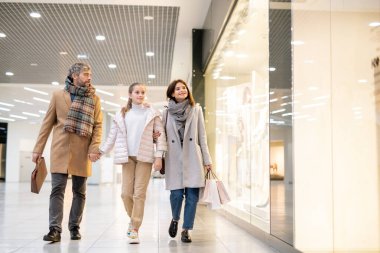 Üç kişilik modern aile alışveriş merkezinin içinde büyük bir dükkan vitrininde yürürken mevsimlik satışın keyfini çıkarıyorlar.