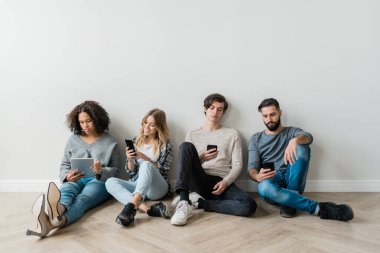 Kültürler arası dört bin yıllık günlük kıyafet beyaz duvarın yanında otururken akıllı telefonlarında kayarken veya mesajlaşırken