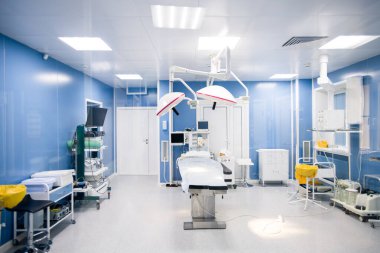 Modern kliniklerdeki cerrahi odasının içinde duvarlar boyunca gerekli tüm ekipmanlar ve üzerinde lambalar olan ameliyat masası.