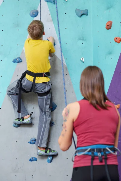 女子インストラクターが近くに立ってロープを保持しながら 積極的に登山の壁に上に移動着用中の女子学生のバックビュー — ストック写真