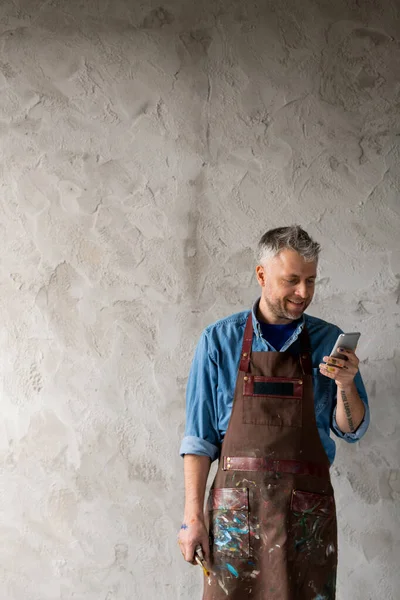 Gelukkige Middelbare Leeftijd Professionele Schilder Werkkleding Stand Muur Scrollen Smartphone — Stockfoto