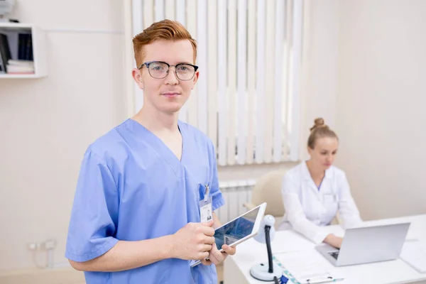 年轻的戴眼镜 身穿蓝色医疗制服的流动实习生站在摄像机前上网 — 图库照片