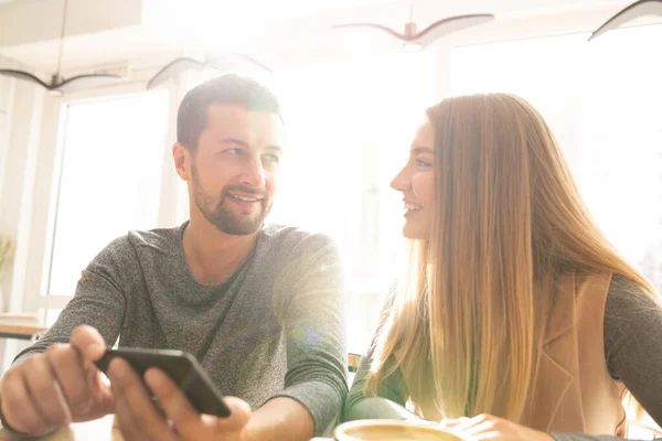 スマートフォンで何かをスクロールしたり見ている間にカフェで面白いことを議論幸せな若い愛情のカップル — ストック写真