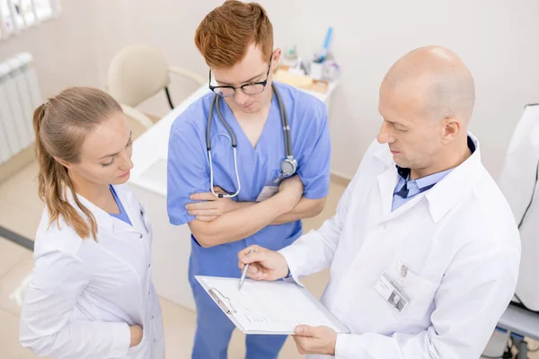 Bald Serious Doctor Whitecoat Pointing Document While Reading Aloud Young — Stock Photo, Image