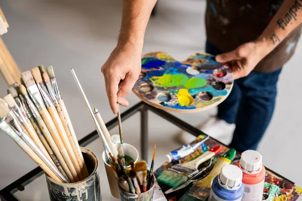 Mãos Pintor Segurando Paleta Com Cores Misturadas Colocando Pincel Vidro — Fotografia de Stock