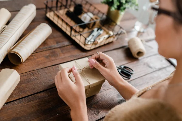 Noel hediyelerini ahşap masadan paketlerken hediye kutusunun üstünde iplik bağlayan genç bir kadının elleri.