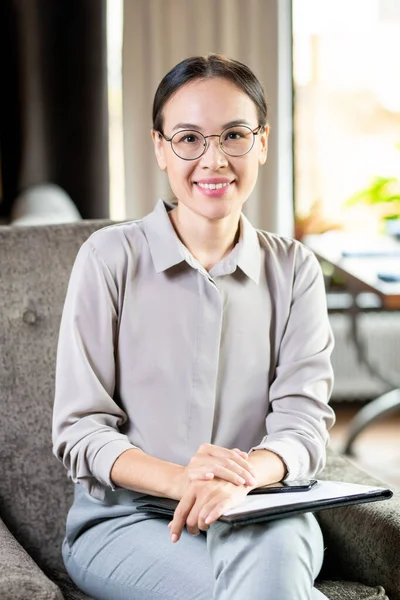 Young elegant successful agent or accountant with documents sitting in armchair in cafe or restaurant