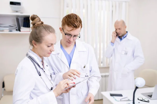 Jóvenes Profesionales Médicos Apuntando Pantalla Táctil Mientras Miran Través Información —  Fotos de Stock