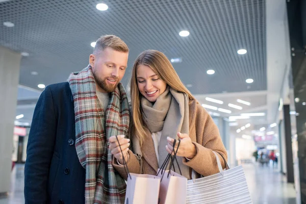 若い笑顔の女性は彼女が一緒に買い物をしながら 彼女が部門の一つで季節の販売で買ったものを夫に示す — ストック写真