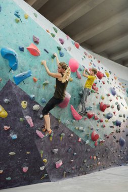Genç, sarışın, aktif bir kadın ve spor giyim bölümünde oğlu boş zamanlarında küçük yapay taşlarla duvara tırmanıyorlar.